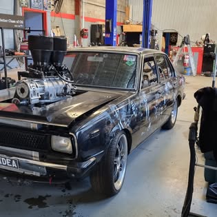 Black Holden Torana with a supercharger protruding through the bonnet, in the R & M bay