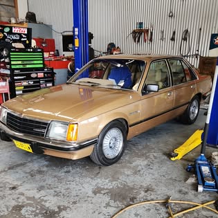 Gold Holden VB Commodore parked in the R & M workshop with hoist and tool wall behind